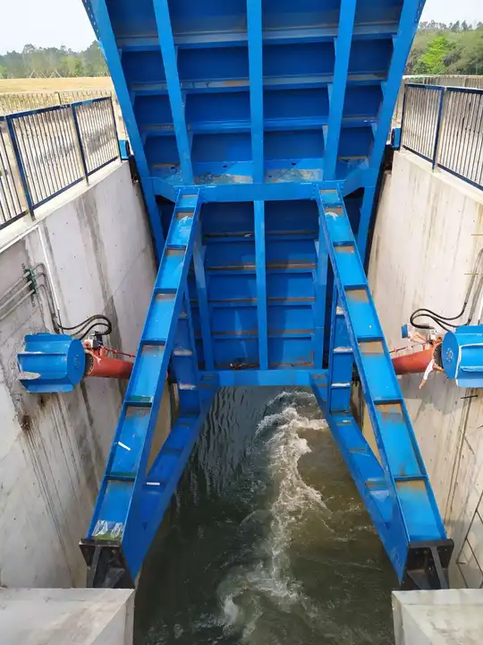 Open blue radial gate with support arms and hydraulic cylinders above flowing water